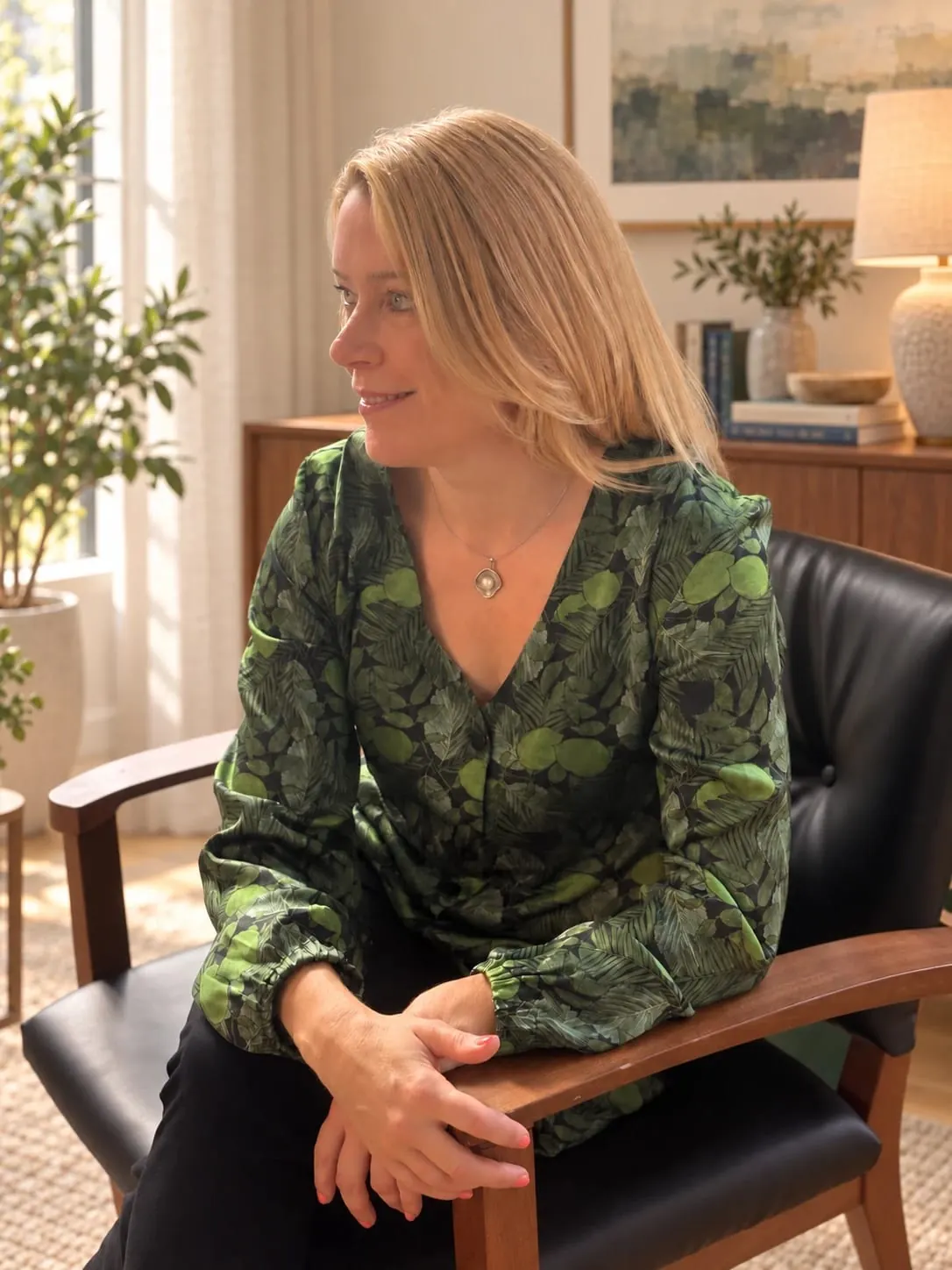 Harriet Parker sitting in a wooden armchair in a sunlit room, looking away from the camera and smiling